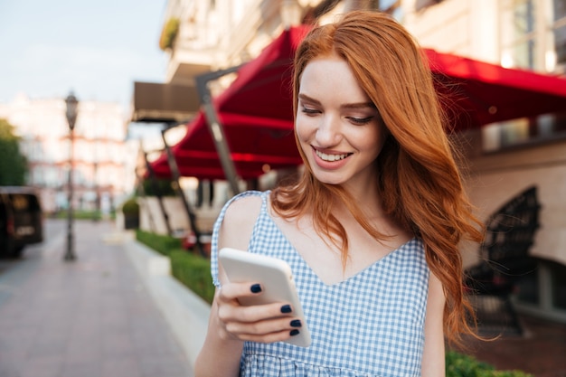 Cheerful redhead woman with long hair using mobile phone while