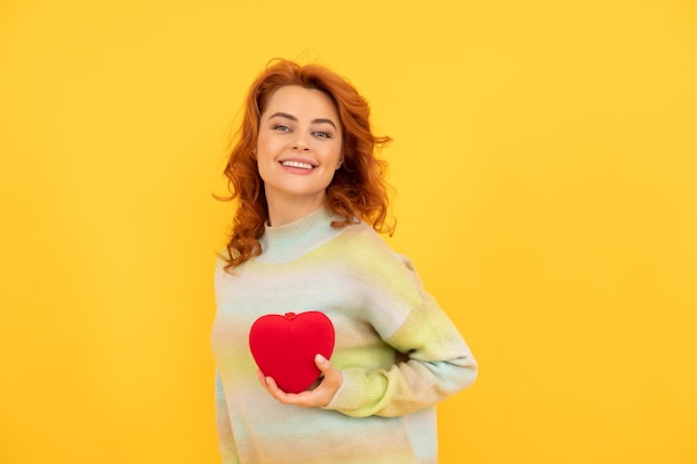 Cheerful redhead woman with red heart on yellow background. love