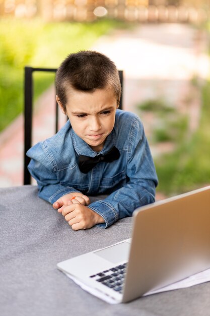 Cheerful schoolboy boy is engaged in lessons through a laptop at home in the garden. Online classes for children