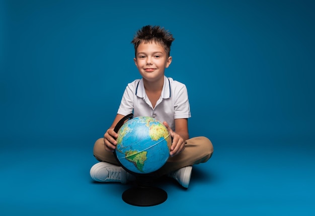 Веселый школьник сидит на синем фоне с рюкзаком и концепцией образования земного шара