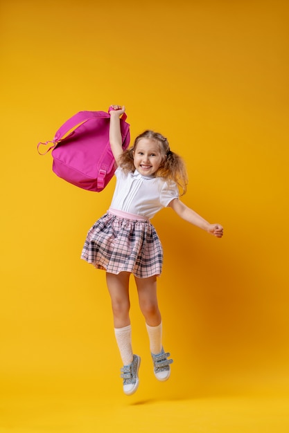 Cheerful schoolgirl in uniform with backpack jumping