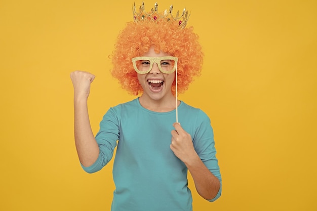 Cheerful selfish child girl in curly wig and princess diadem wear party glasses success