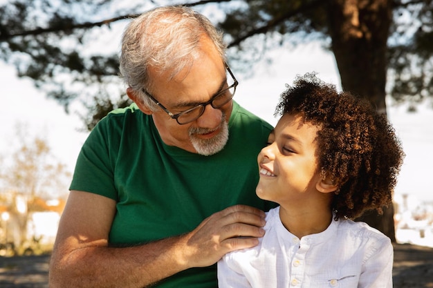 Cheerful senior caucasian grandfather hugging little mixed race boy talking enjoy free time fun