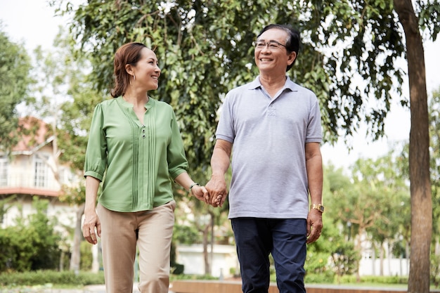 Cheerful senior couple holding hands when walking outdoors in city park having romantic date