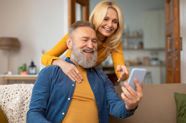 Cheerful senior couple using mobile phone sitting at home