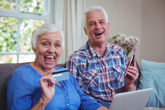 Cheerful senior couple with credit card and technology 