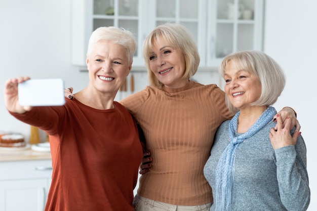 Cheerful senior ladies taking selfie together using smartphone