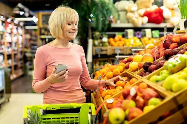 Cheerful senior lady customer purchasing at store using phone