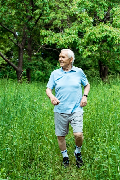 Cheerful senior man with grey hair running in green park