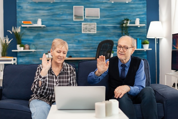 Cheerful senior man and woman waving during online call with family