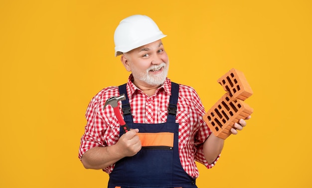 Cheerful senior man worker in helmet on yellow background