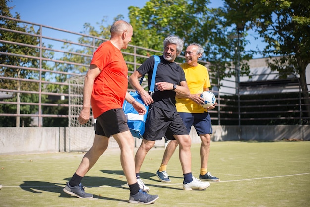 Uomini senior allegri prima della partita. uomini con i capelli grigi in abiti sportivi in piedi sul campo sportivo, preparandosi a giocare a calcio. concetto di calcio, sport, tempo libero