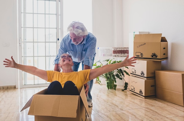 Cheerful senior people in empty room playing like children in\
relocation happy for new beginning like retired with moving boxes\
on the floor