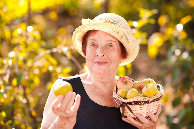 Cheerful senior woman holding basket with green apples