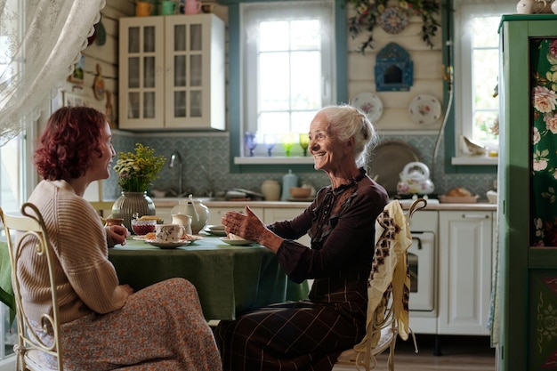 Photo cheerful senior woman in smart casualwear chatting with her granddaughter