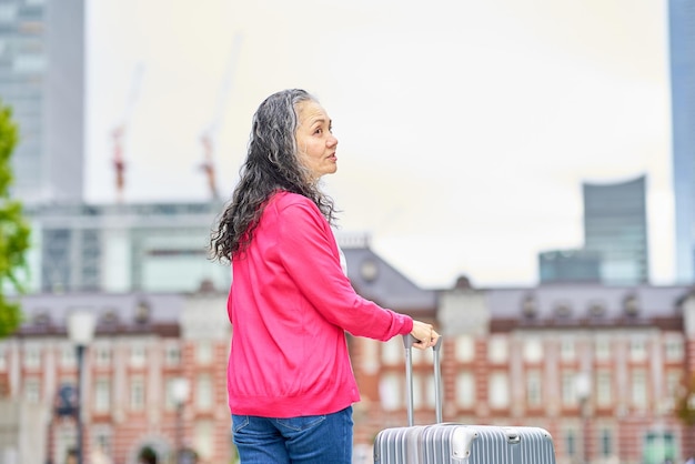 Cheerful senior woman walking around the city with a suitcase