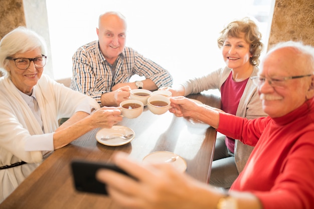 Cheerful seniors photographing together while drinking tea