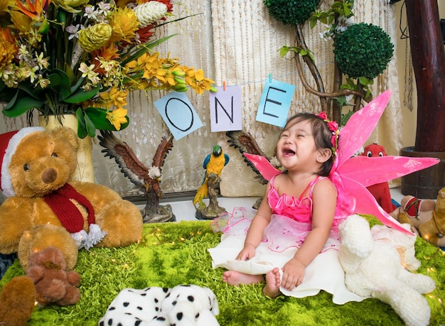 Cheerful shirtless baby girl sitting amidst stuffed toys during birthday