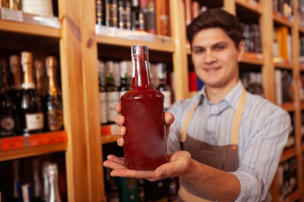 Cheerful shopkeeper smiling holding out bottle to the camera, copy space