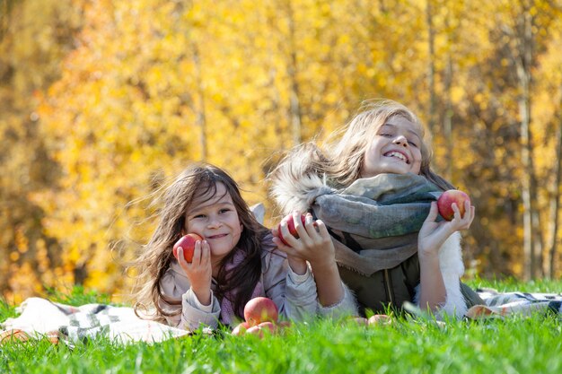 Cheerful sisters holding apples on autumn picnic