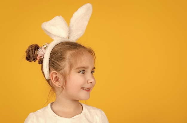 Cheerful small easter girl in bunny ears on yellow background copy space