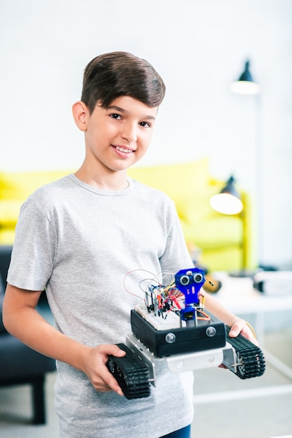 Cheerful smart little boy holding his robot while showing the result of his work