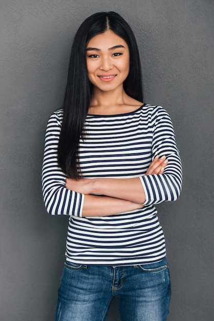 Cheerful smile. Beautiful young Asian woman keeping arms crossed