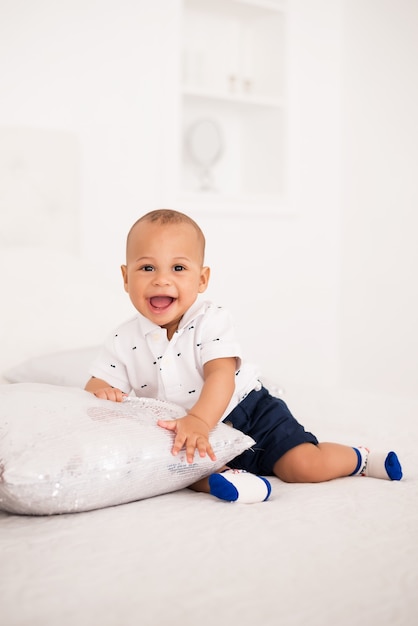 Cheerful smiling african american baby sitting on the bed.