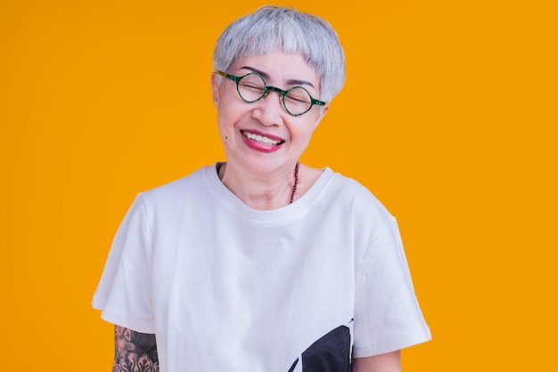 Cheerful smiling asian senior woman wear glasses grey hair in casual cloth portrait headshot on yellow color background