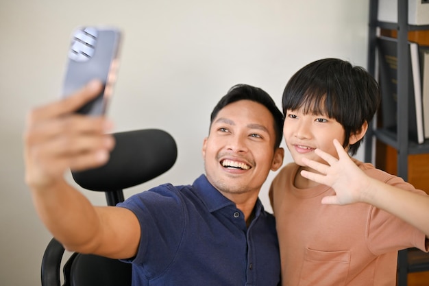 Cheerful and smiling Asian son and dad are taking a picture together with smartphone