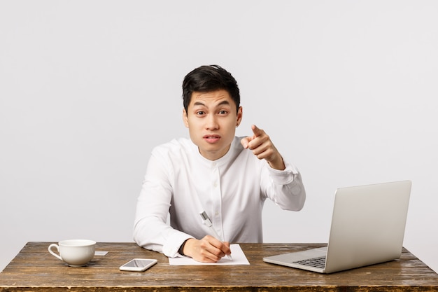 Cheerful smiling asian young entrepreneur pointing at the office