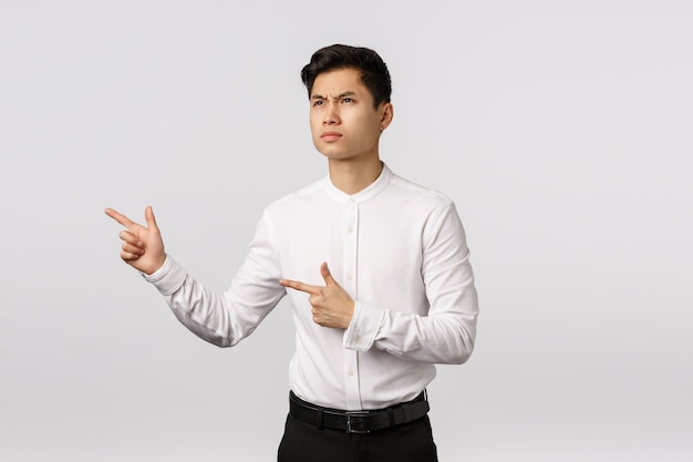 Cheerful smiling asian young entrepreneur with white shirt pointing to the side