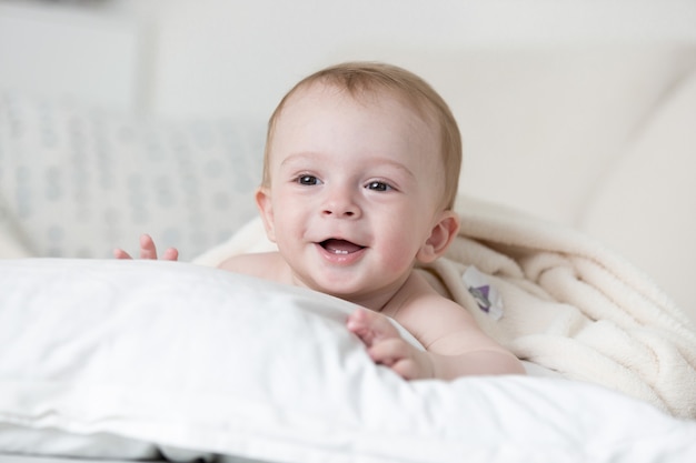 Cheerful smiling baby boy relaxing on big white pillow on bed