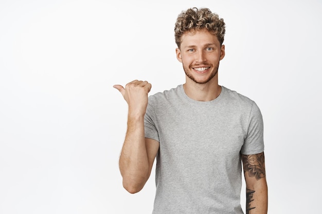 Cheerful smiling blond man pointing left showing direction way to sale banner white backgroung wearing casual grey tshirt