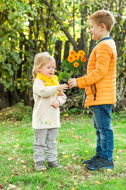 写真 黄色のジャケットを着た陽気な笑顔の少年は、自然の中で黄色のスカーフを着た少女に花をプレゼントします