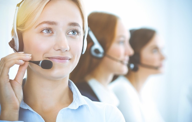 Cheerful smiling business woman with headphones consulting clients. Group of diverse phone operators at work in sunny office.Call center and business people concept.