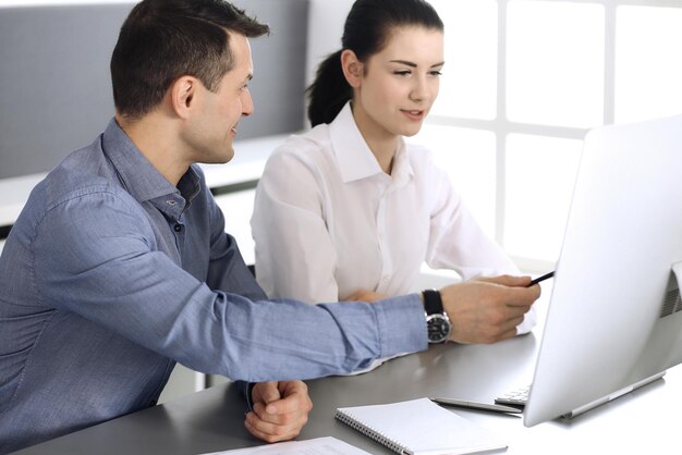 Cheerful smiling businessman and woman working with computer in modern office. Headshot at meeting or workplace. Teamwork, partnership and business concept.