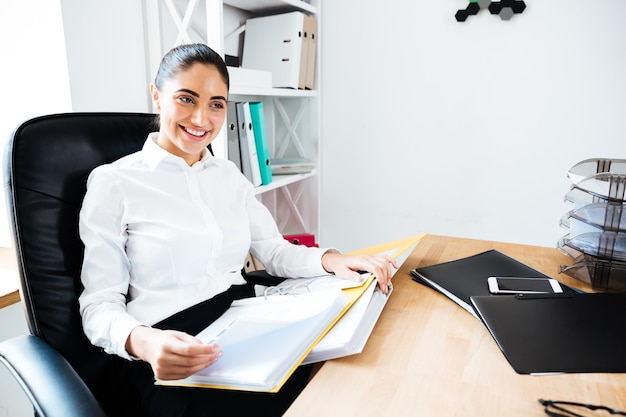 Photo cheerful smiling businesswoman reading documents while sitting at the office desk