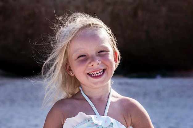 ビーチで水着姿の陽気な笑顔の子ブロンドの女の子