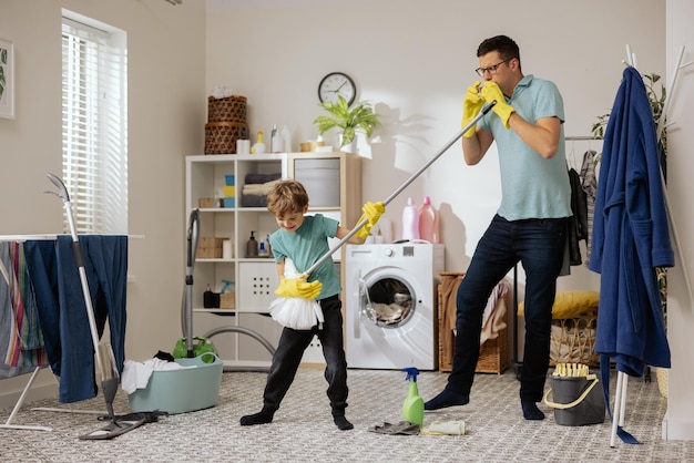 A cheerful smiling father and son help each other mop the floor with a mop and bucket