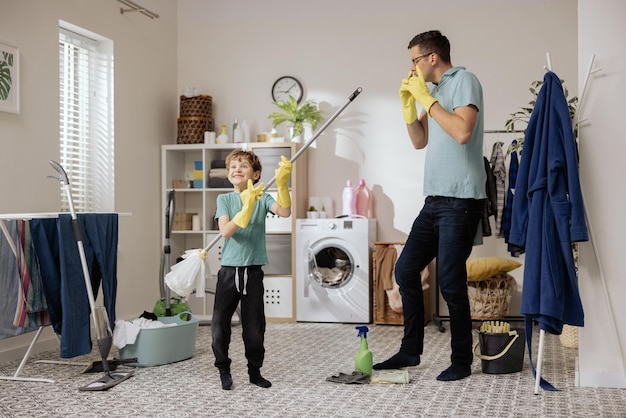 A cheerful smiling father and son help each other mop the floor with a mop and bucket