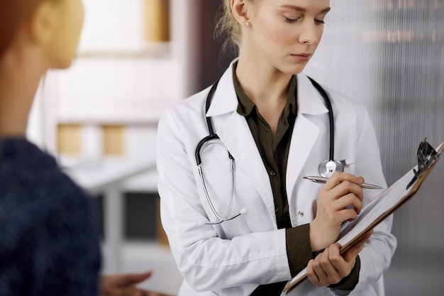 Cheerful smiling female doctor and patient woman discussing current health examination while sitting in sunny clinic Perfect medical service in hospital Medicine concept