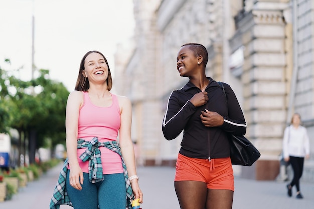 Cheerful smiling friends in sportswear walking after a sport session in the city discussing and having fun Multiethnic women having a fitness workout jogging