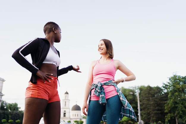 Cheerful smiling friends in sportswear walking after a sport session in the city discussing and having fun Multiethnic women having a fitness workout jogging