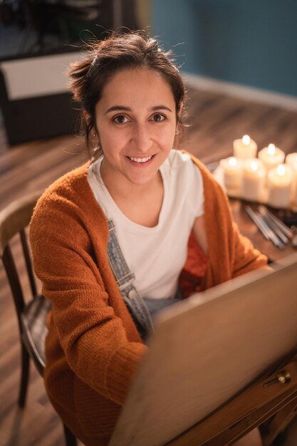 Photo a cheerful smiling girl is drawing a new picture while sitting in a chair in her living room