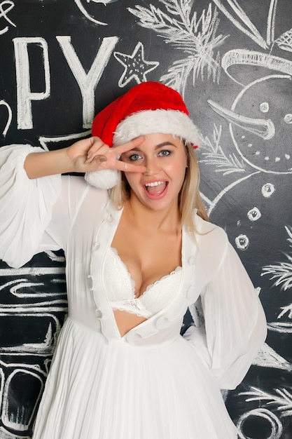 cheerful smiling girl in santa claus cap with Christmas writings on a chalkboard