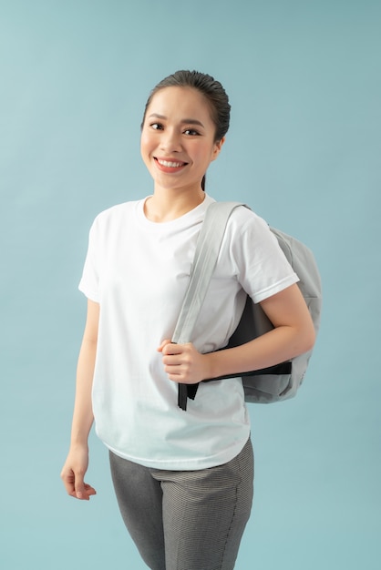 A cheerful, smiling girl with charming long hair with a gray backpack on her back, isolated on a blue background.