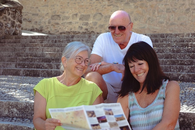 Веселая улыбающаяся группа пожилых людей, сидящих на лестницах и смотрящих на концепцию путешествия по туристической карте