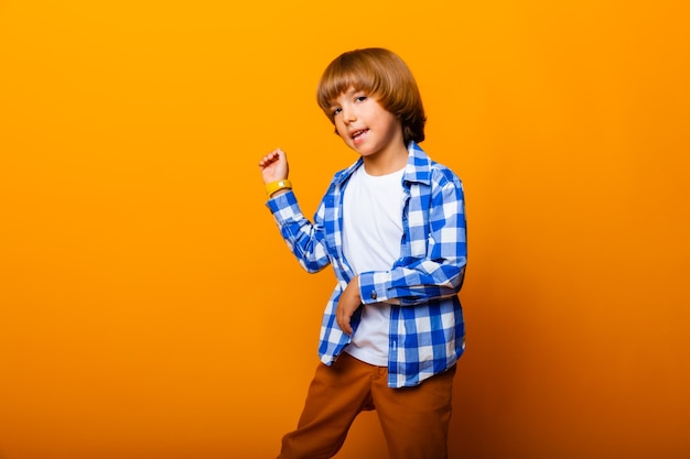 Cheerful smiling little boy jumping and having fun at the yellow wall. School concept.