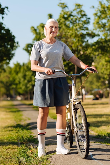 彼女の自転車の近くに立っている陽気な笑顔の年配の女性